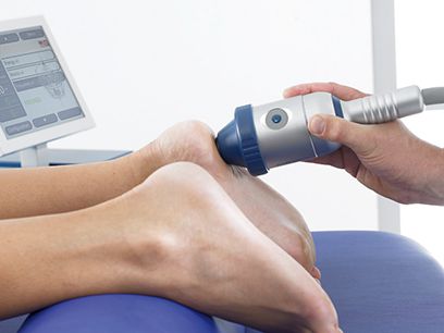 Dieses Bild zeigt die Anwendung der Stoßwellentherapie an den Füßen eines Patienten